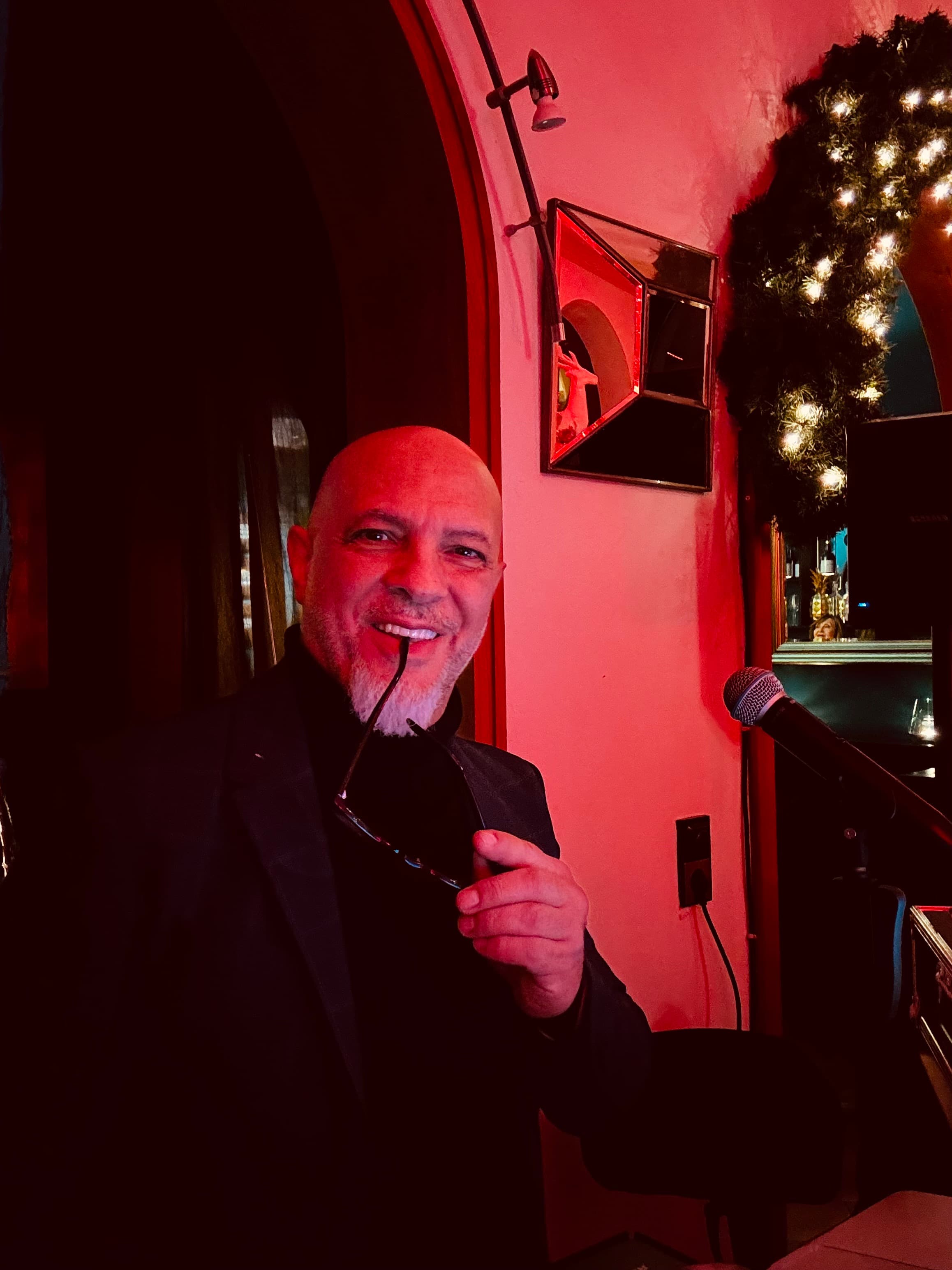 Marco Serra mit Mikrofon und Sonnenbrille vor warmer roter Bar-Beleuchtung